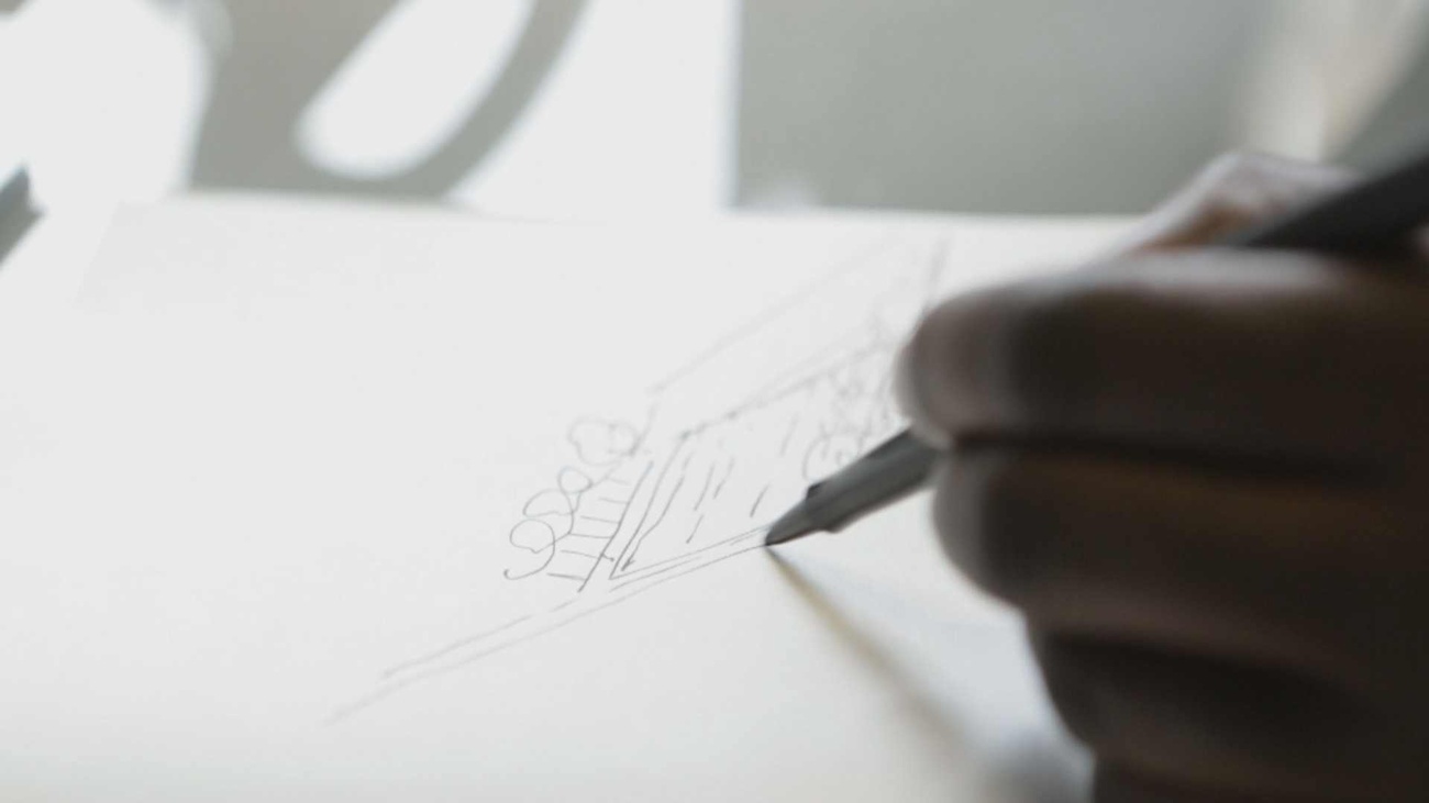 The hand of a Black individual holding a pencil and drawing an architectural sketch. Film Still by Oliver Hardt